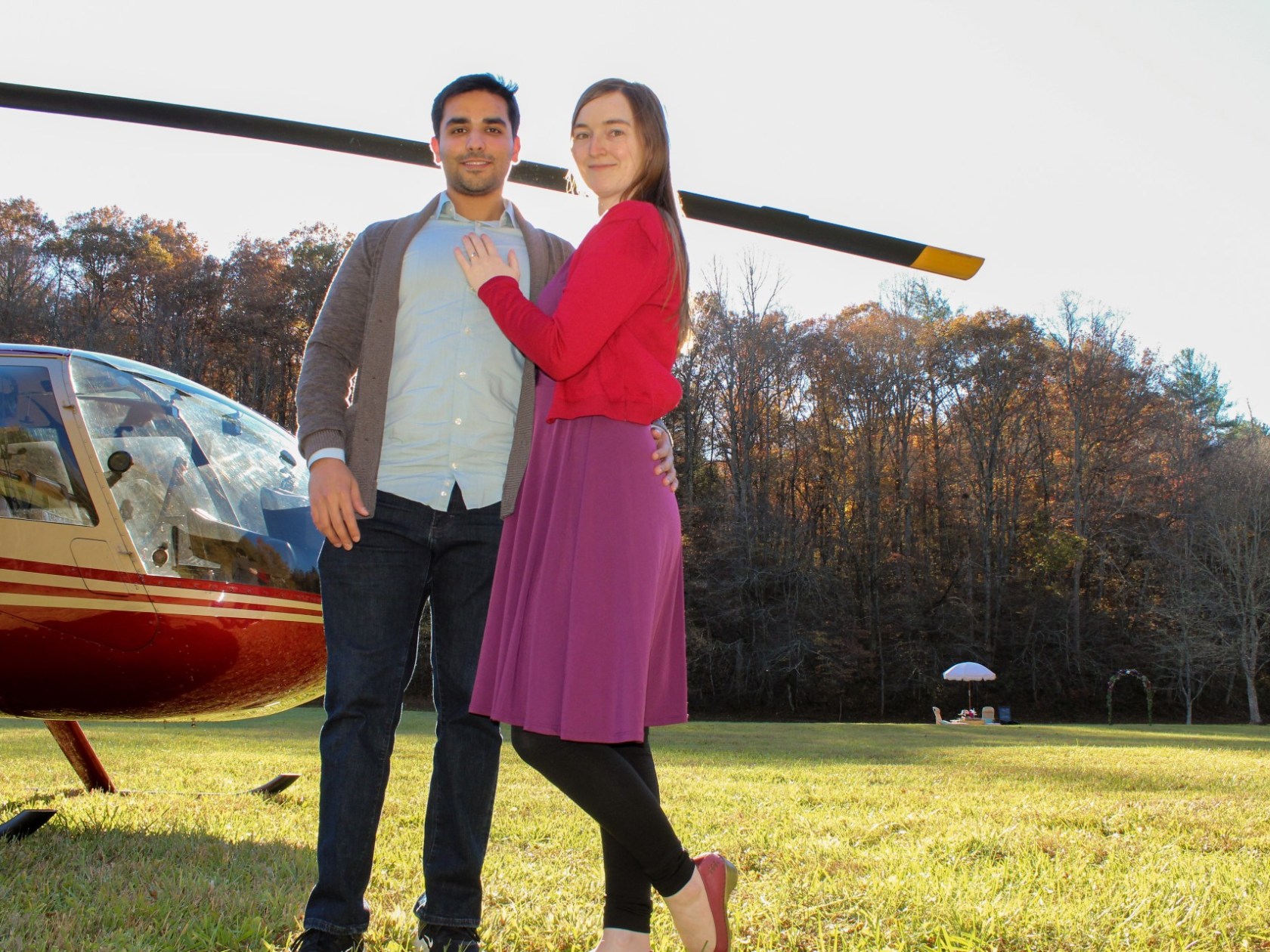 a couple standing in a field near a helicopter