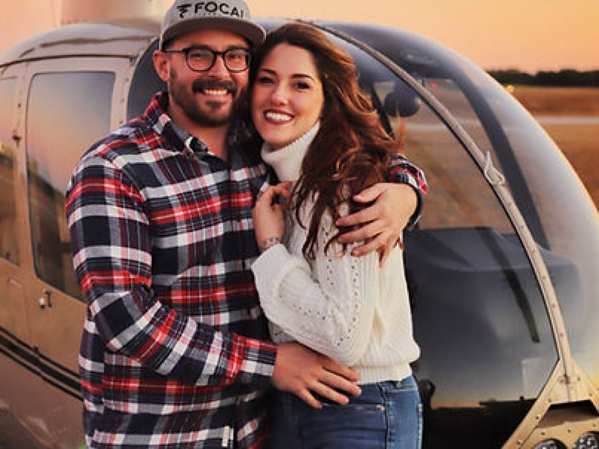 a couple standing in front of a helicopter